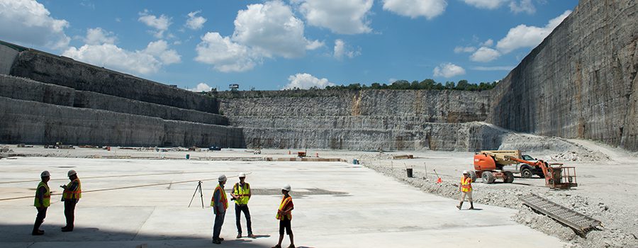Three men in yellow vests standing on a cement field.