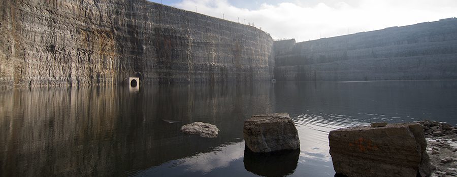 A rock in the middle of a lake near a cliff.