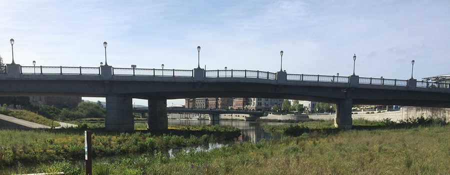A bridge over water with grass and trees in the background.